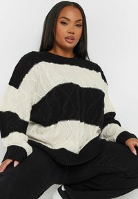 Svart och krämfärgad stickad tröja med kabelstickat mönster, som har breda ränder samt ribbad krage och mudd. Kombineras med svarta byxor.