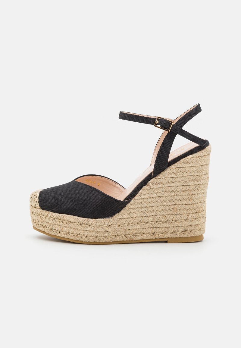 Sandalias de cuña de tela negra con tacón de yute trenzado, puntera redonda y correa al tobillo con detalle de hebilla dorada. Diseño fácil de poner con un forro interior suave.
