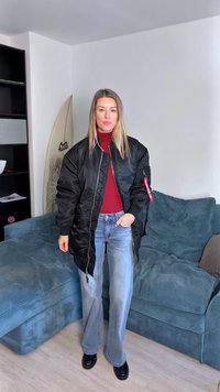 Svart bomberjakke med en blank finish, ribbestrikkede mansjetter og sideglidelåser. Brukt over en rød genser med høy hals og kombinert med lyseblå flagrende jeans.