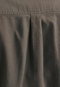 Tejido gris oscuro con una sutil textura, que presenta un detalle de pliegue recogido cerca de la parte superior, creando un suave drapeado.
