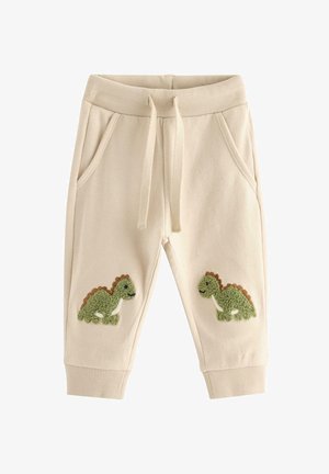 Beige sweatpants til småbørn med ribbet talje og manchetter, snøre, sidelommer og grønne dinosaur-patches på knæene.
