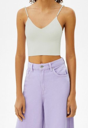 Woman wearing a ribbed white cropped top with thin straps and high-waisted wide-leg lavender jeans against a white background.