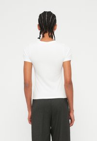 T-shirt bianco a maniche corte con collo rotondo, texture liscia, design aderente e senza motivi visibili, abbinato a pantaloni grigio scuro.