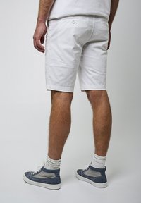 Pantalones cortos de algodón blancos con un corte relajado, que presentan dos bolsillos traseros y un cierre de botón. Combinados con zapatillas deportivas altas azules y calcetines blancos.