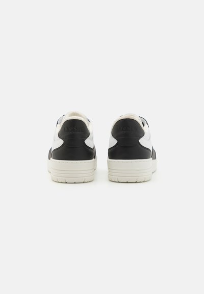 White and black leather sneakers with textured finish, featuring a flat white sole, rounded toe, padded collar, and Moschino logo on the heel.