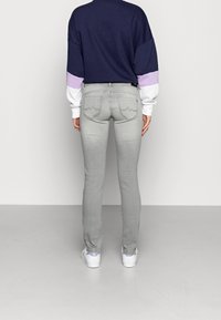 Šedé slim-fit džíny s hladkou strukturou a jemným detailem na zadních kapsách, spárované s mikinou v námořnické modré a levandulové barvě s barevnými bloky.