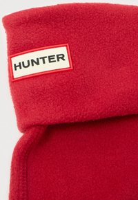 Rød fleece-stoff med en brettet kant, som har et rektangulært merke med hvit bakgrunn og svart skrift som sier "HUNTER."