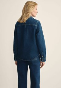 Jeansowa kurtka o luźnym kroju, ciemnoniebieski kolor, zapięcia na guziki na rękawach oraz kontrastowe detale szwów.