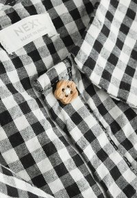 Un tissu à carreaux vichy noir et blanc présentant un bouton en bois en forme de fleur et une étiquette portant la mention "NEXT MADE IN INDIA."