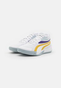 Chaussures de sport blanches à tige en mesh, avec des accents violets et jaunes, un bout arrondi et une semelle épaisse grise.