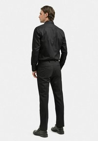 Svart långärmad skjorta med en mjuk textur, i kombination med skräddarsydda svarta byxor. Båda plagg har en slimmad passform och minimal detaljer.