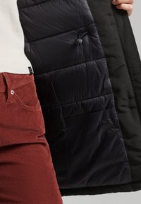 Black insulated jacket with a smooth, shiny interior and textured exterior. Features adjustable drawstring and side pockets.