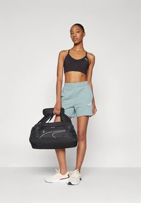 Svart sportbehå, ljusblå shorts och vita sneakers som bärs av en person som håller en svart sportväska med vita detaljer och mönstrade handtag.