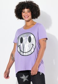 T-shirt violet à manches courtes avec un grand graphique de visage souriant argenté. Le t-shirt a une coupe décontractée et un col arrondi.