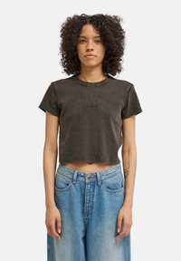 Κοντομάνικο σκουρόχρωμο γκρι t-shirt με κυματιστή υφή και κοντά μανίκια, με κεντημένο λογότυπο στο μπροστινό μέρος, συνοδευόμενο από ανοιχτόχρωμο τζιν παντελόνι.