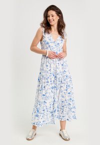 Robe maxi blanche avec imprimé floral et motifs scéniques bleus, bretelles à volants, jupe à volants et décolleté en V profond. Assortie avec des baskets.