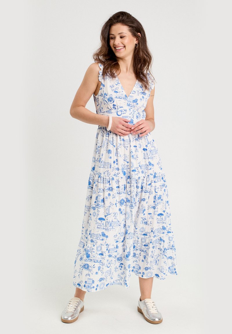 Robe maxi blanche avec imprimé floral et motifs scéniques bleus, bretelles à volants, jupe à volants et décolleté en V profond. Assortie avec des baskets.