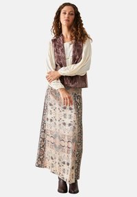 Chaleco burdeos de terciopelo sobre una blusa crema, combinado con una falda larga de patrón floral en colores suaves, usada con botas marrones.