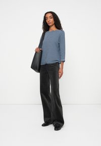 Striped navy and white long-sleeve top paired with wide-leg black corduroy pants and holding a black tote bag. Flat black shoes complete the look.