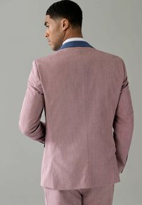 Helles rosa maßgeschneidertes Sakko mit strukturierter Oberfläche. Besitzt einen kontrastierenden blauen Kragen und ein schlankes Design.