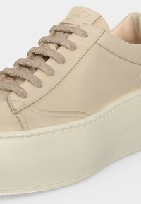 Gros plan d'une basket beige à plateforme avec de larges lacets texturés et une semelle lisse et arrondie, avec des détails cousus près des orteils.