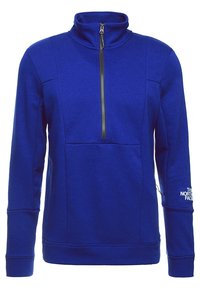 Modrý fleecový pulovr s vysokým límcem, polovičním zipem vpředu a dlouhými rukávy. Má prošitou panelovou konstrukci a logo na levém rukávu.