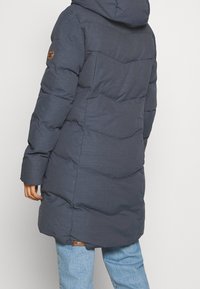 Vadderad mörkgrå vinterjacka med huva, i en chevrondesign, långa ärmar och en logotypapplikation på vänster arm.