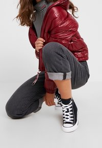 Rød, skinnende vinterjakke med hætte, grå bukser med opslag og sorte højhælede sneakers. Under jakken er der en stribet rullekrave.