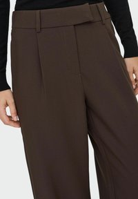 Braune maßgeschneiderte Hose mit weit geschnittenem Design, gefaltenem Vorderteil und hohem Bund mit Gürtelschlaufen. Glattes Material mit feiner Nahtverarbeitung.