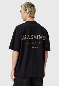 Zwarte oversized t-shirt met metallic gouden luipaardprint tekst op de achterkant, met de tekst "ALLSAINTS" en "LONDEN." Eenvoudige, relaxte pasvorm.