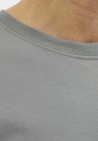 Lys grå bomulds t-shirt med ribbet rund halsudskæring og glat tekstur, med synlige søm langs kanterne.