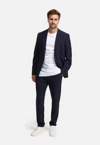 Completo blu navy realizzato in tessuto textured, abbinato a una t-shirt bianca e sneakers bianche, caratterizzato da una vestibilità moderna e un design sartoriale.