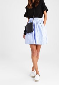 Svart kortärmad topp, ljusblå och vit randig kjol med elastisk midja, svart crossbody-väska med tofs och vita espadrilloskor.