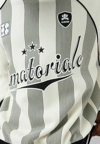 Sudadera a rayas blancas y negras con el logo "matoriale", tres estrellas y parches con una textura suave y cuello redondo.