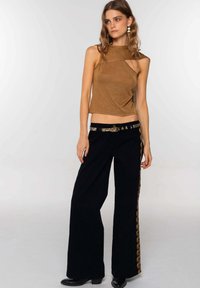 Top sin mangas dorado metálico con un diseño asimétrico combinado con pantalones negros de pierna ancha de cintura alta, con un cinturón decorativo y detalles laterales.