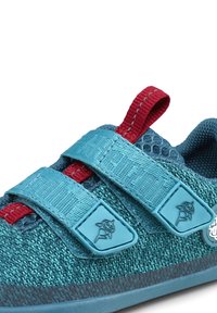 Scarpa sportiva turchese con tessuto a rete, due cinturini blu regolabili, dettagli rossi, suola testurizzata e un'etichetta con logo grigia sul lato.