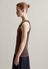 Brauner ärmelloser Top mit taillierter Form und V-Ausschnitt. Aus weichem Material gefertigt, hat er ein schlichtes Design und eine glatte Textur, kombiniert mit einem dunkelblauen Rock.