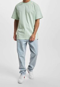 Jasnozielony, prążkowany t-shirt z okrągłym dekoltem, zestawiony z jasnoniebieskimi, luźnymi dżinsami i białymi trampkami z czerwonymi akcentami.