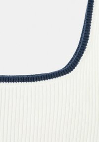 Tissu côtelé blanc avec une bordure côtelée bleu marine le long du bord arrondi de l'encolure.