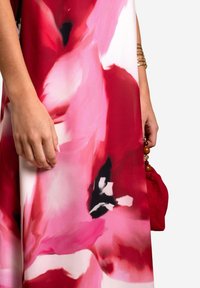 Rotes und pinkes Kleid mit Blumenmuster aus leichtem Stoff; verfügt über eine seidige Textur und einen fließenden Schnitt, ergänzt durch eine rote Handtasche.