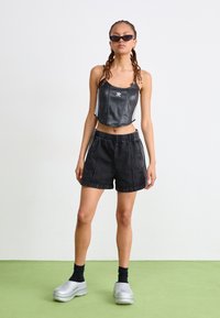 Top de couro preto cropped com riscas brancas, combinado com calções de ganga pretos e sapatos slip-on prateados. A modelo usa meias pretas e óculos de sol.