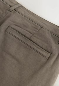 Pantalons en coton gris dotés d'une poche arrière avec un rabat rectangulaire, une texture lisse et un subtil détail de couture sur la ceinture.