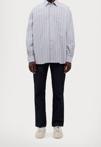 Camisa de botones en azul claro con rayas blancas verticales, bolsillo en el pecho, mangas largas; combinada con jeans de mezclilla oscuros y zapatillas beige.