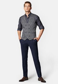 Szary kamizelka w kratę na ciemnej koszuli, w połączeniu z granatowymi spodniami na miarę i brązowymi sznurowanymi butami. Skupienie na czystych liniach i dopasowanym kroju.