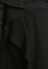 Vêtement noir avec un ourlet à volants et une bordure en dentelle délicate. Texture de tissu lisse ; design en couches ajoutant de la profondeur et un intérêt visuel.