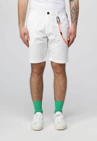 Pantaloni corti bianchi in cotone con risvolti, dotati di un bottone nero e una corda decorativa arancione e nera sul lato. Sneakers bianche e calze verdi.