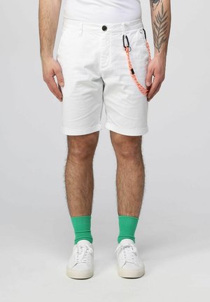 Pantaloni corti bianchi in cotone con risvolti, dotati di un bottone nero e una corda decorativa arancione e nera sul lato. Sneakers bianche e calze verdi.