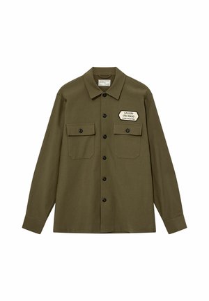 Olivengrøn skjorte med knapper og krave, to brystlommer med klapper og en hvid lap med teksten "Gallery Ltd. Tokyo Studio Collection."