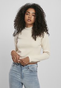Krämfärgad långärmad topp med en mock-neck, som har en figursydd design och slät textur, ihop med ljusblå denimjeans.