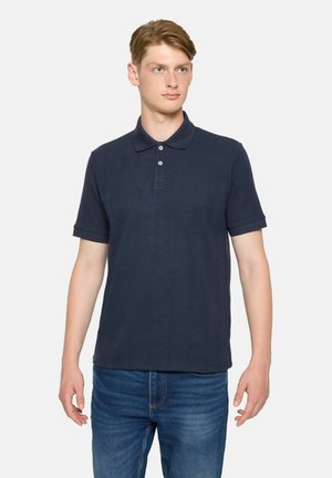 Marineblaues Polohemd mit strukturiertem Muster, kurzen Ärmeln und einer Knopfleiste mit drei Knöpfen. Kombiniert mit Jeans.